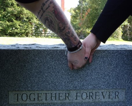 holding hands over a tombstone that reads 'together forever'